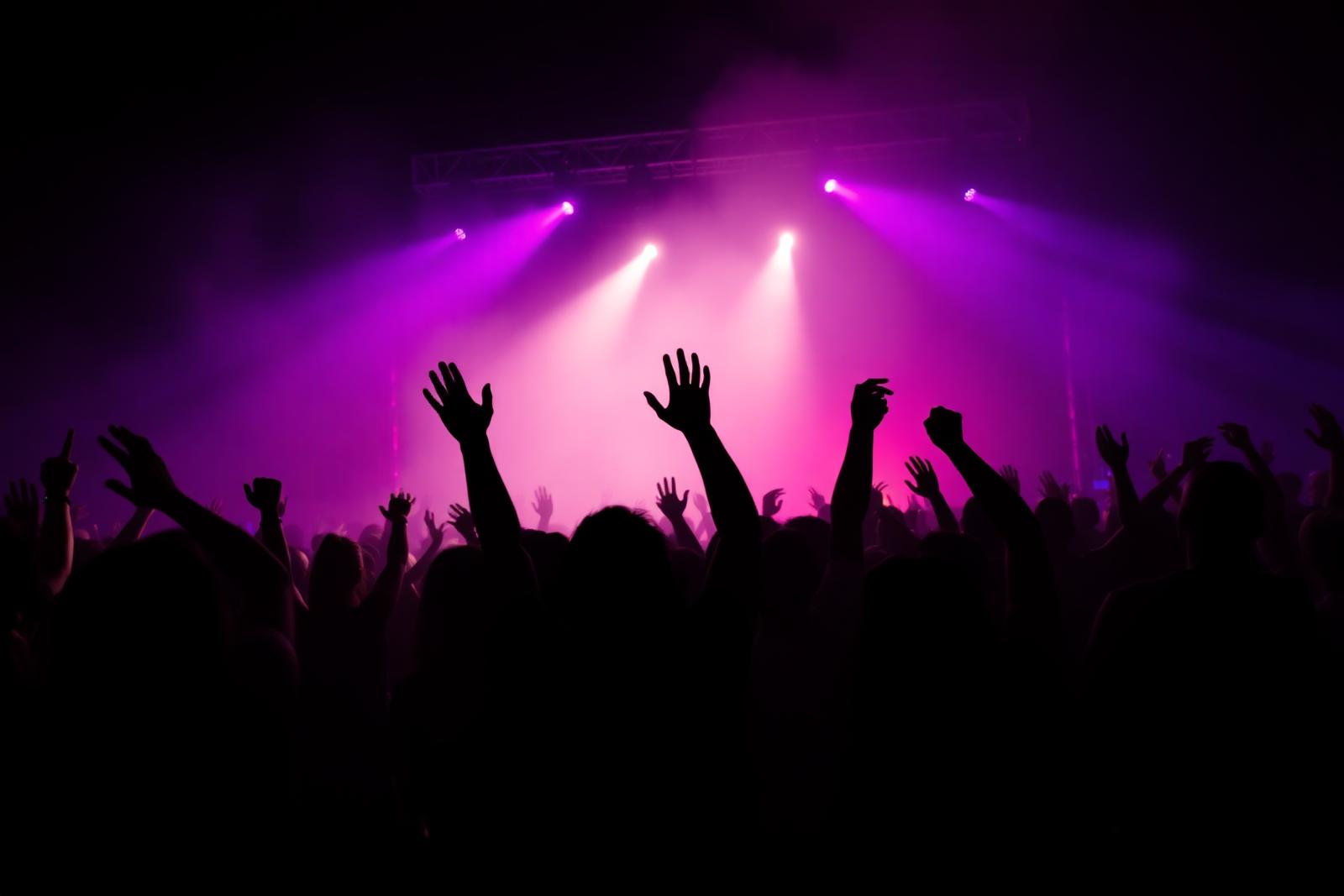 Festival crowd with raised hands bathed in purple and pink stage light
