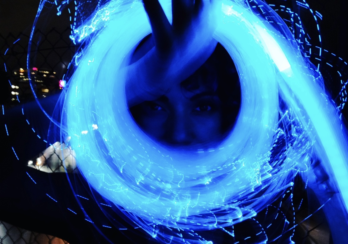 Luna Chi framed by a swirling blue LED light whip trail at night
